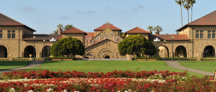 Stanford campus with rows of beautiful flowers in a courtyard and buildings connected by archways and palm trees in the distance